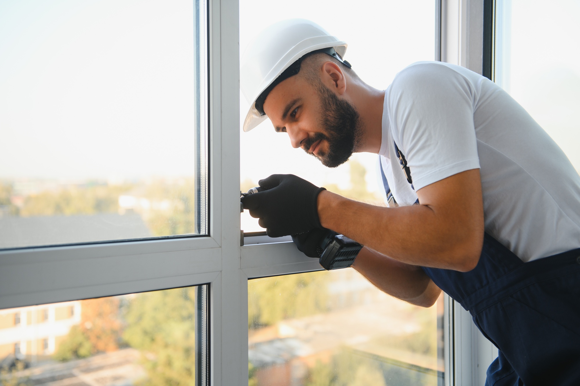 Workman in overalls installing or adjusting plastic windows in the living room at home